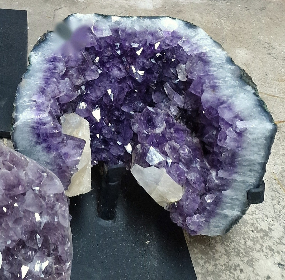 Amethist geode met paarse kristallen en witte calciet op een zwarte standaard